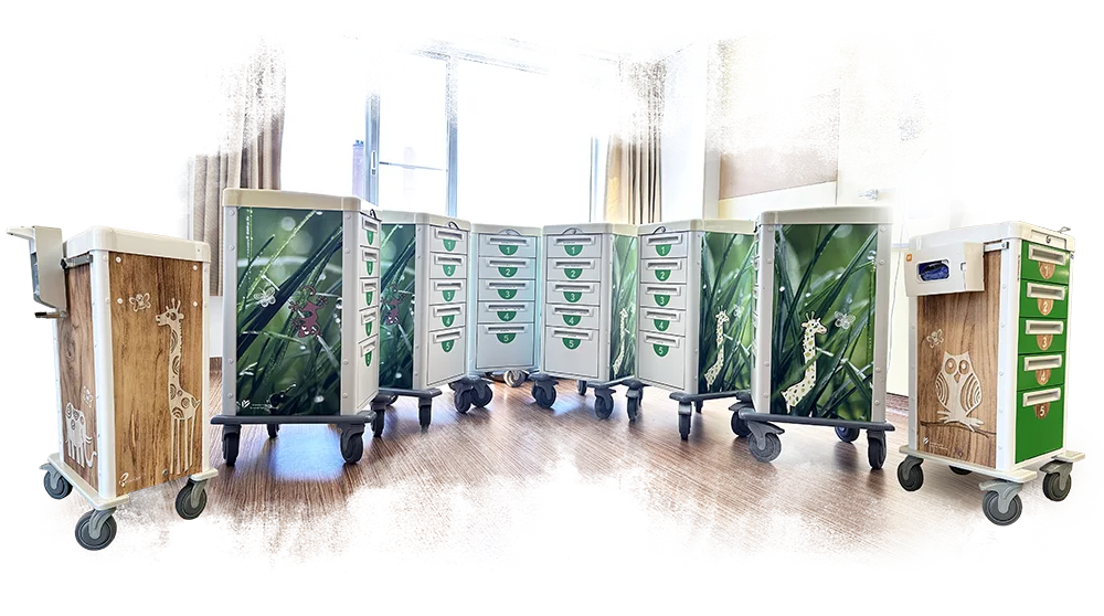 Een rij medische karren in het Groene Hart Ziekenhuis, gezellig gewrapt met houtprints, graspatronen en vrolijke getekende dieren zoals een uil en giraf.